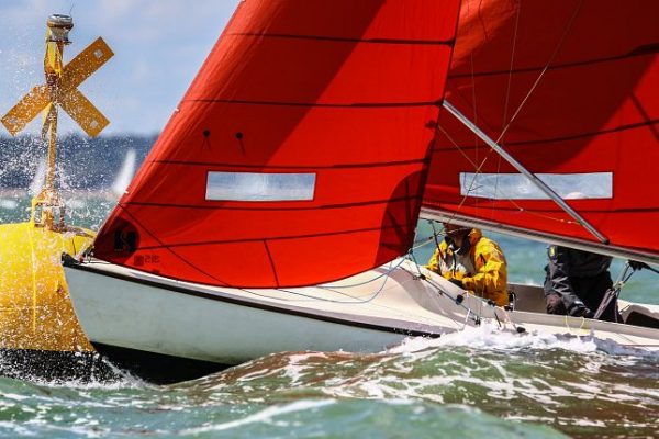 A white yacht with a red sail passes a buoy during Cowes Week