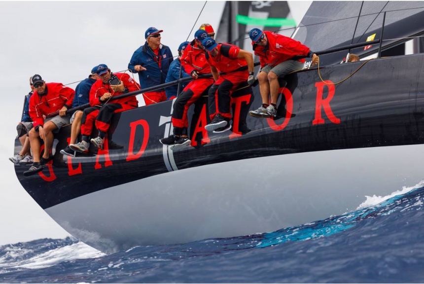 Sailors dressed in red hang over the edge of a sailing monohull yacht