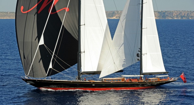 An expensive sailing yacht with a red and black hull and red, white and black sails